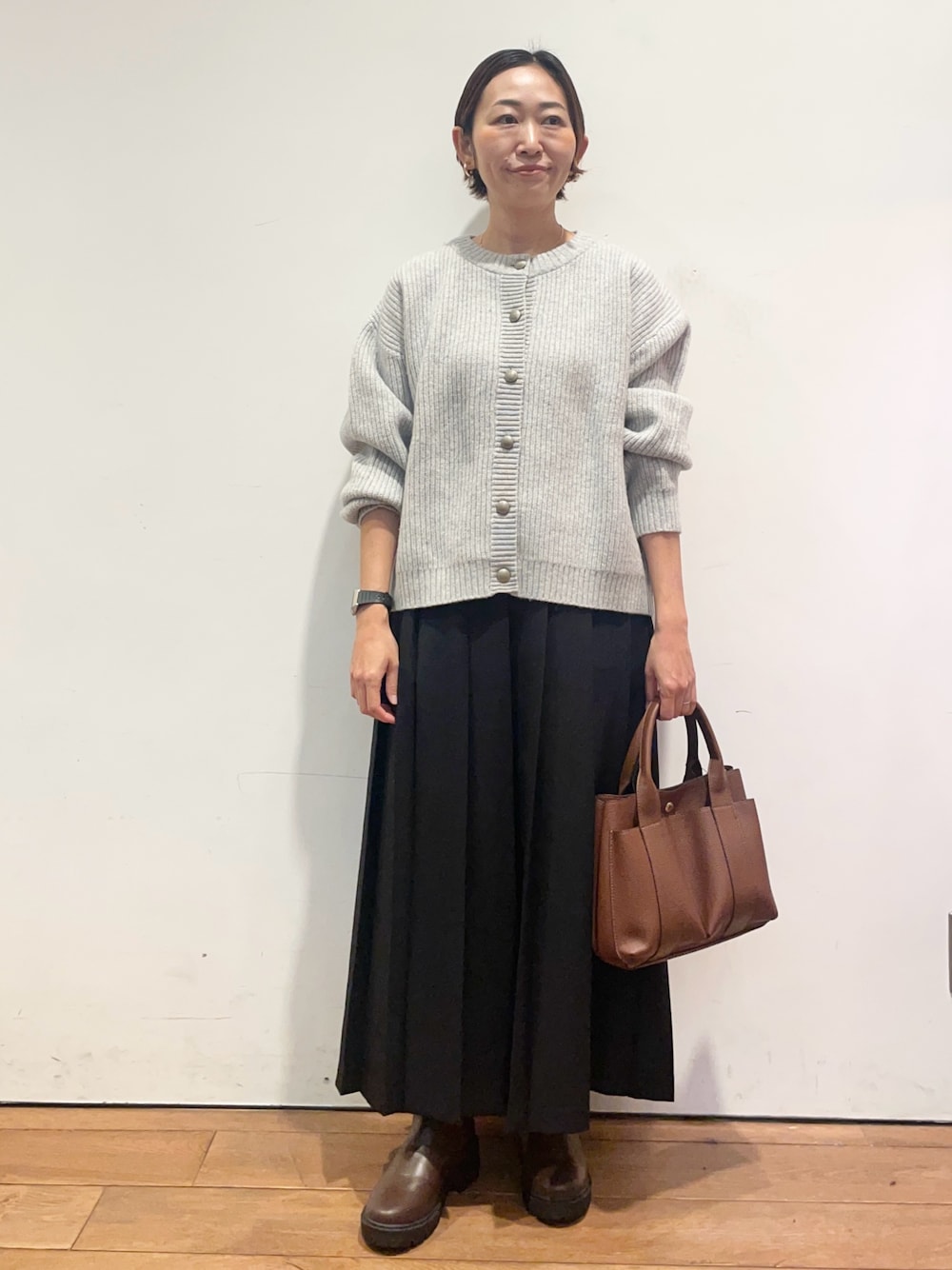 ブラック系のスカート、ブラウン系のトートバッグ、ブラウン系のブーツを着用したレディースの秋コーディネートの1枚目の写真