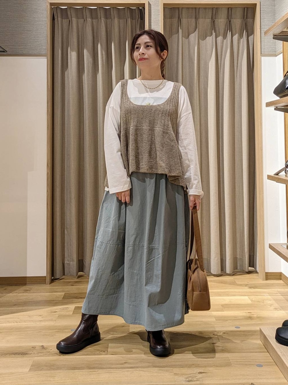 ブラウン系のショルダーバッグ、ブルー系のスカート、ブラウン系のブーツを着用したレディースの秋コーディネートの1枚目の写真
