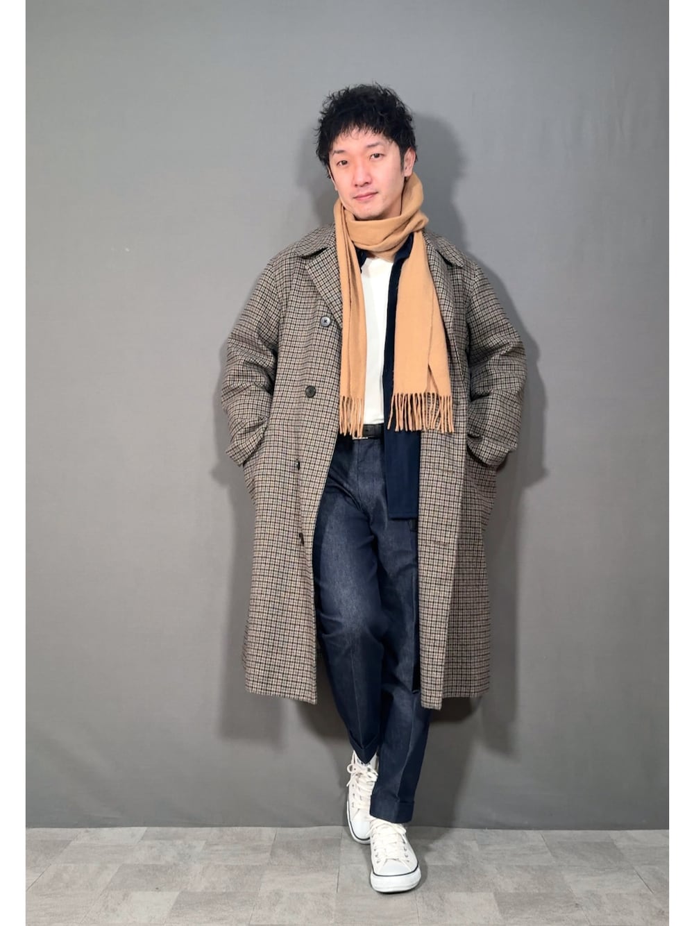 ベージュ系のステンカラーコート、ブルー系のデニムパンツ、ホワイト系のスニーカーを着用したメンズの冬コーディネートの1枚目の写真