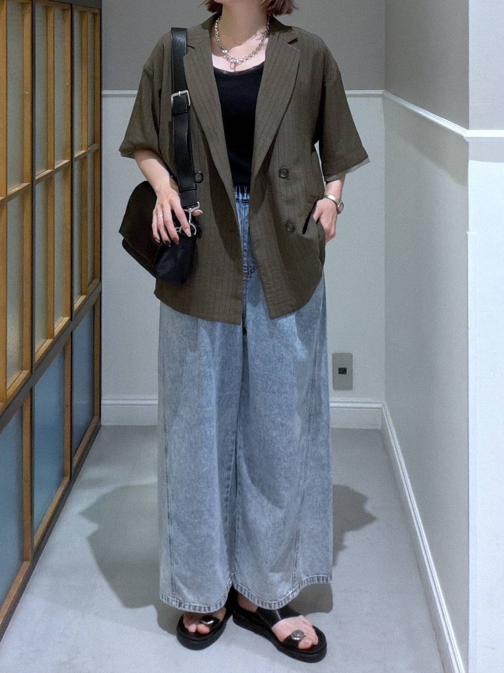 ブラック系のショルダーバッグ、ブルー系のデニムパンツ、ブラック系のサンダルを着用したレディースの春コーディネートの1枚目の写真