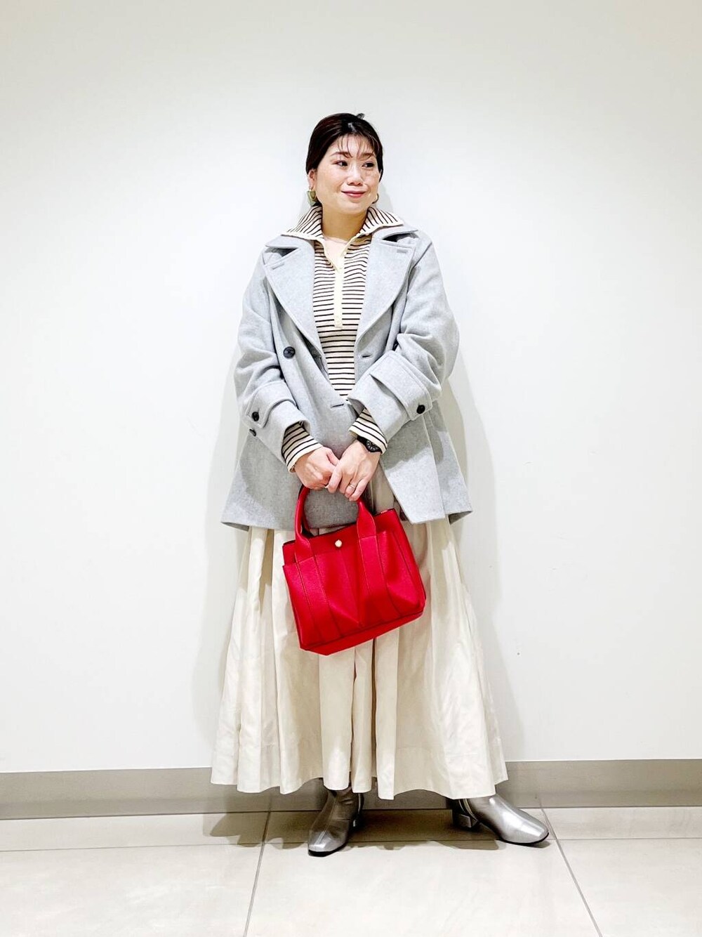 グレー系のピーコート、レッド系のトートバッグ、ホワイト系のニット/セーターを着用したレディースの秋コーディネートの1枚目の写真
