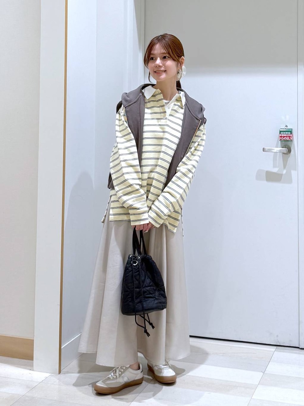 ホワイト系のスニーカー、ブラック系のハンドバッグ、ベージュ系のスカートを着用したレディースの春コーディネートの1枚目の写真