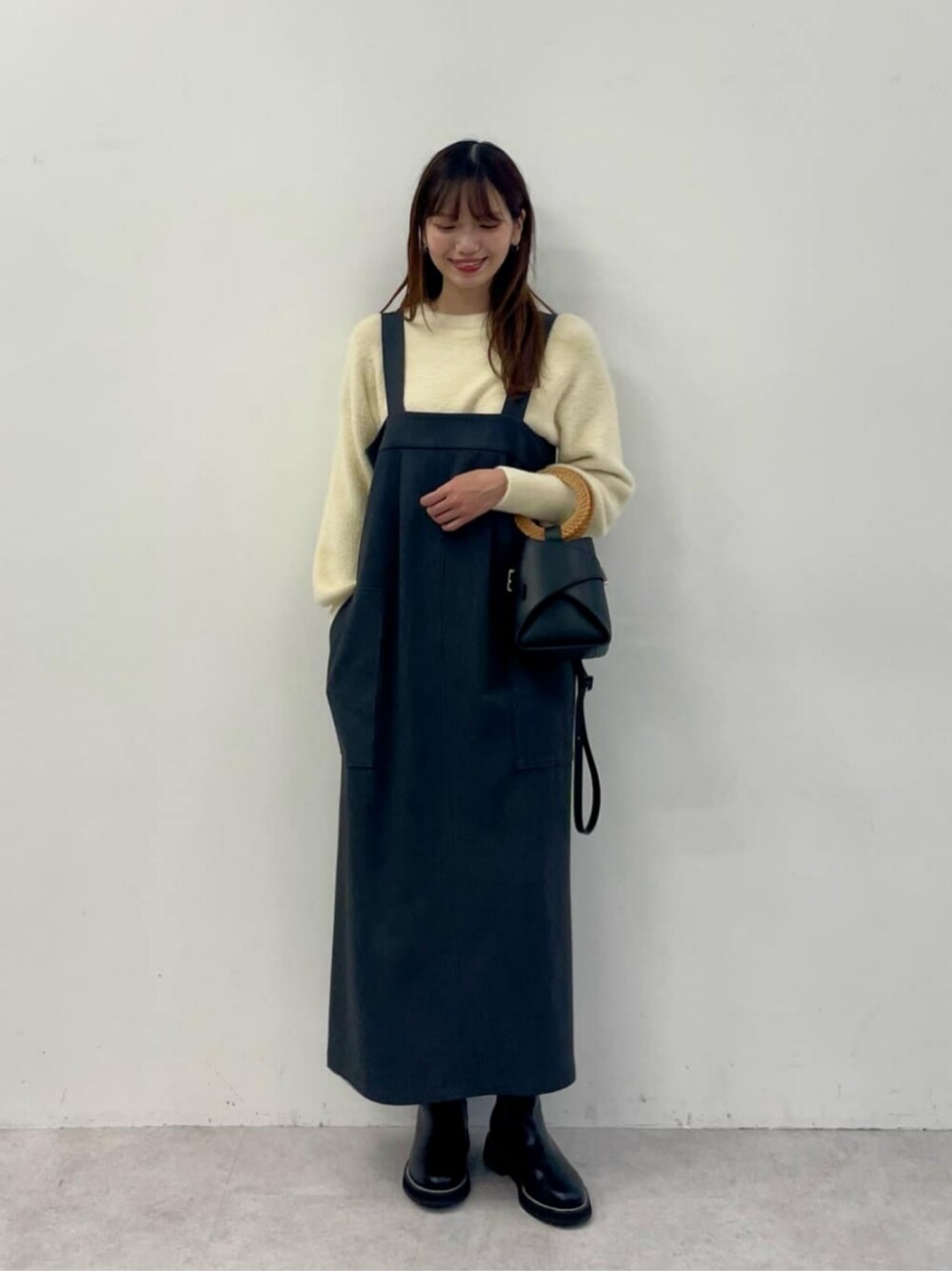 その他のブーツ、ベージュ系のニット/セーター、グレー系のジャンパースカートを着用したレディースの冬コーディネートの1枚目の写真