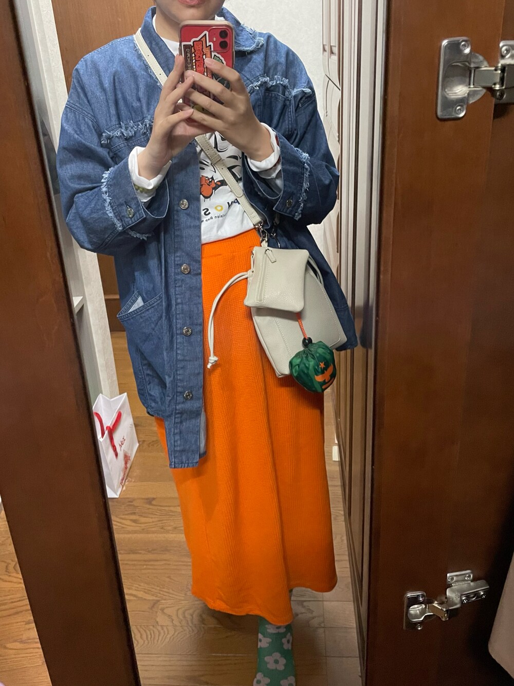 オレンジ系のスカート、ブルー系のデニムジャケット、ホワイト系のショルダーバッグを着用したレディースの春コーディネートの1枚目の写真