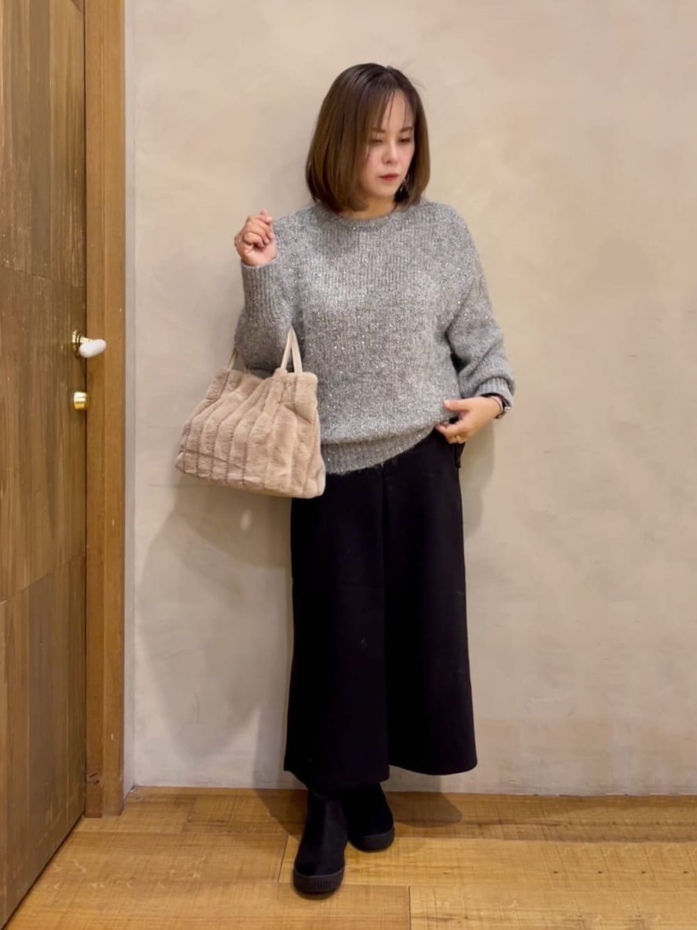 グレー系のニット/セーター、ブラック系のブーツ、ベージュ系のトートバッグを着用したレディースの冬コーディネートの1枚目の写真