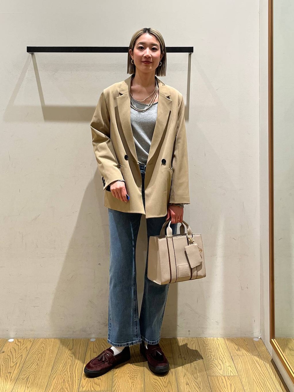 ベージュ系のハンドバッグ、ベージュ系のテーラードジャケット、ブルー系のデニムパンツを着用したレディースの冬コーディネートの1枚目の写真