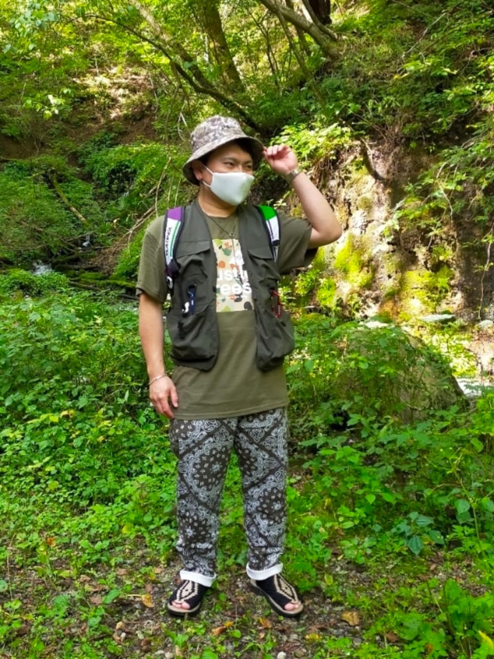 「Tシャツ、フィッシングベスト、バケットハット、ペイズリー柄パンツ、チュバスコ、リュック」｜「LRGの【LRG】カモフラ柄プリント 半袖Tシャツ（Tシャツ/カットソー、グリーン系）」を使った、小林一寿さん（メンズ・166cm）の秋コーディネートの1枚目の写真
