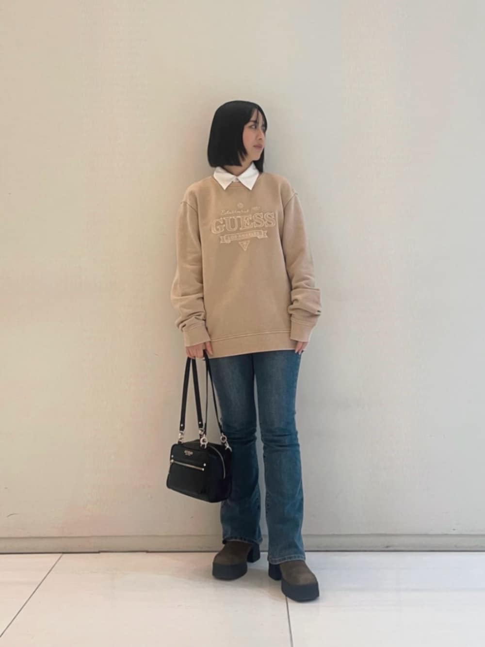 ブルー系のデニムパンツ、ベージュ系のポロシャツ、ブラック系のショルダーバッグを着用したレディースの冬コーディネートの1枚目の写真