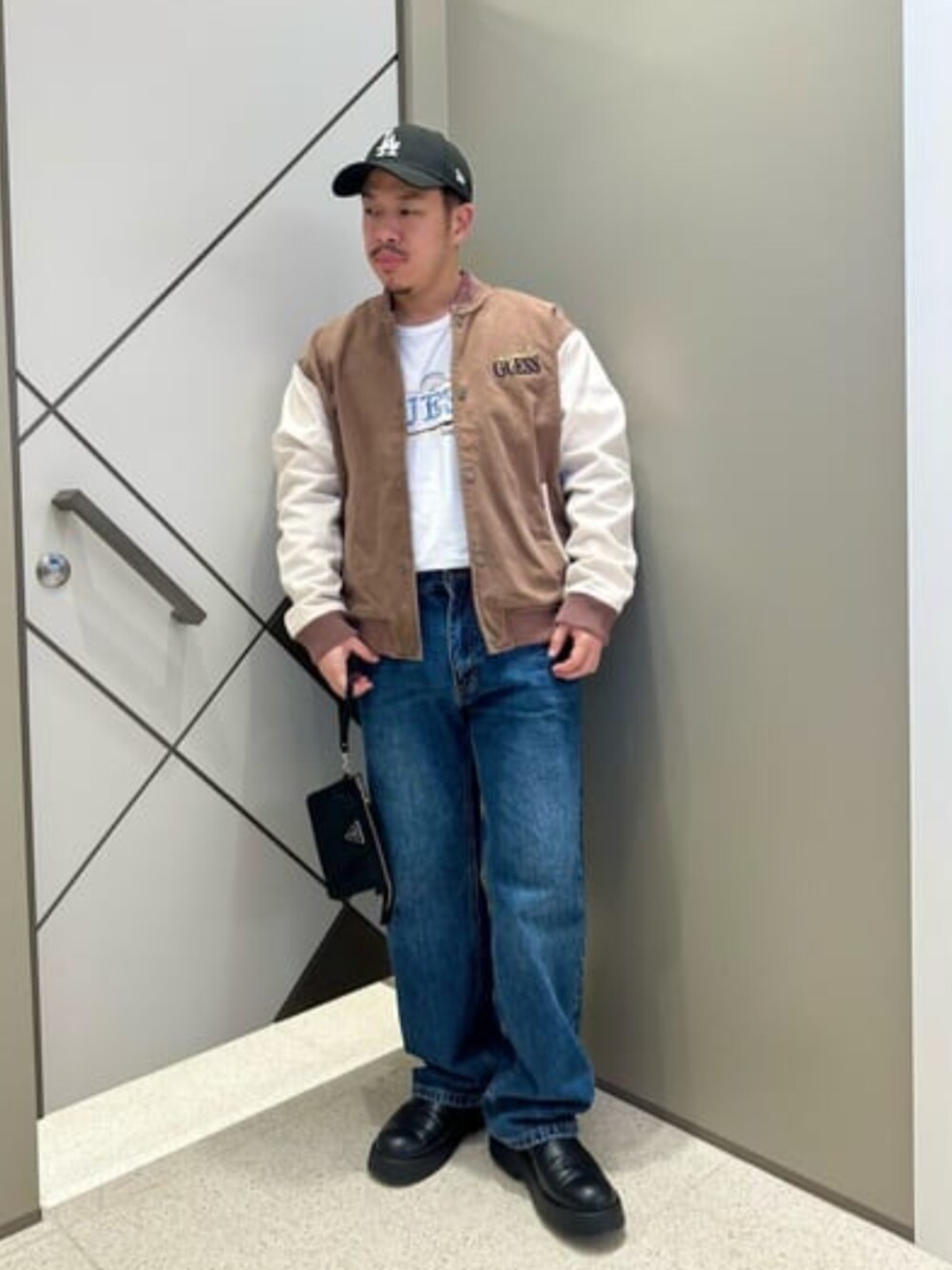 ブラウン系のスタジャン、ブルー系のデニムパンツ、ブラック系のショルダーバッグを着用したメンズの夏コーディネートの1枚目の写真