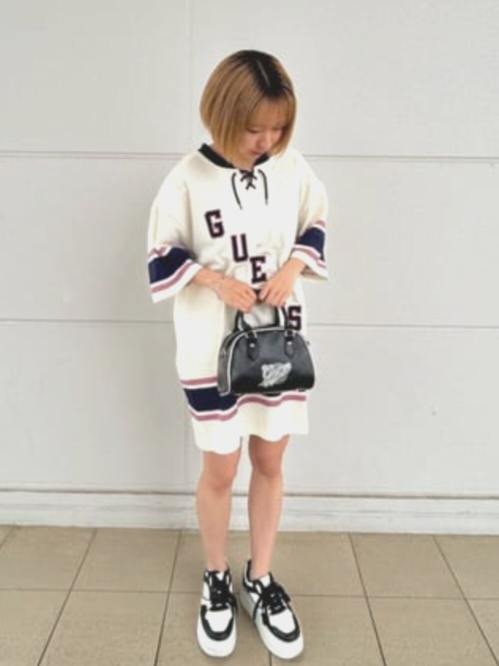 ブラック系のハンドバッグ、ホワイト系のワンピースを着用したレディースの夏コーディネートの1枚目の写真