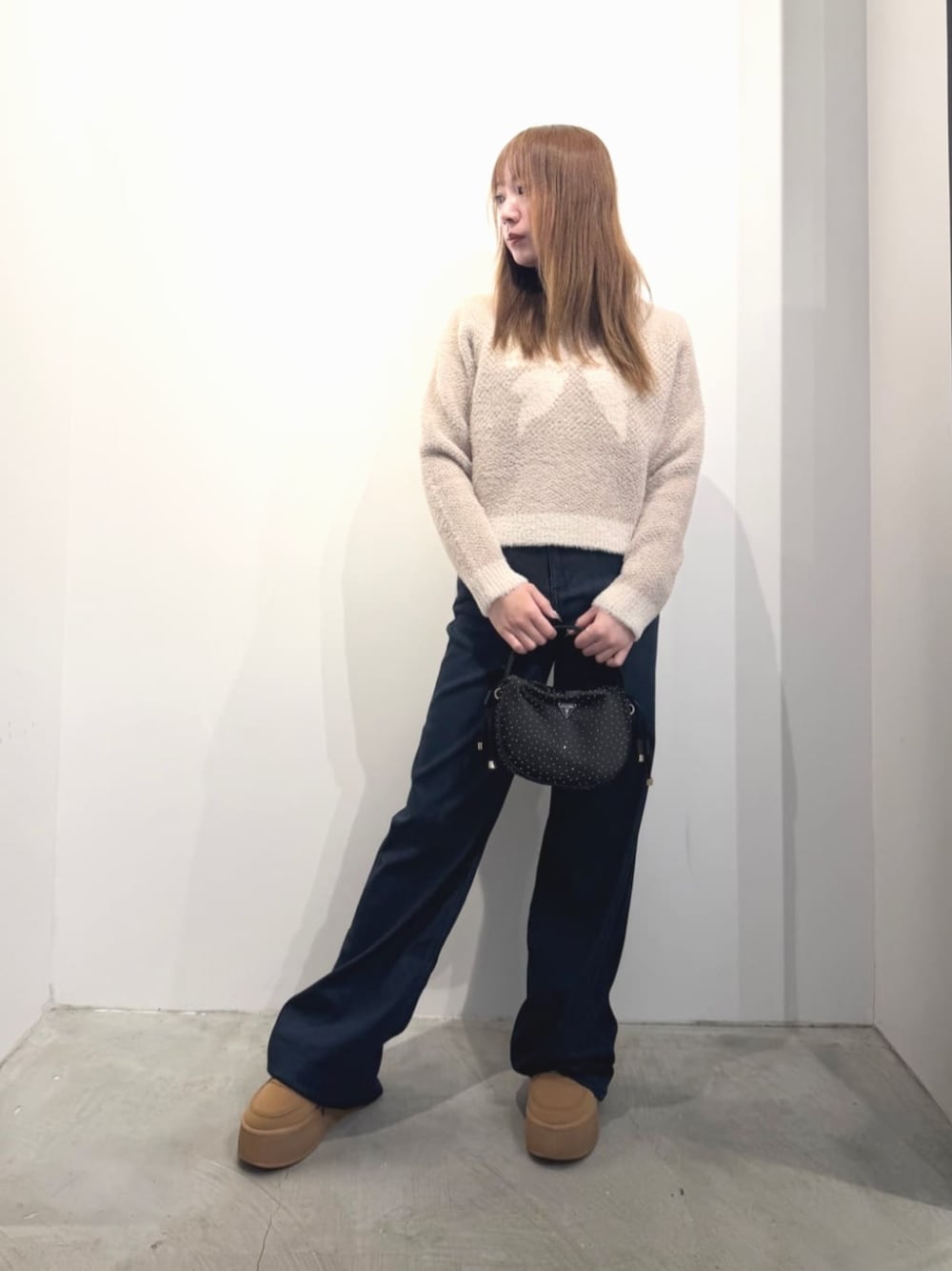 ブルー系のデニムパンツ、ベージュ系のニット/セーター、ブラック系のハンドバッグを着用したレディースの春コーディネートの1枚目の写真