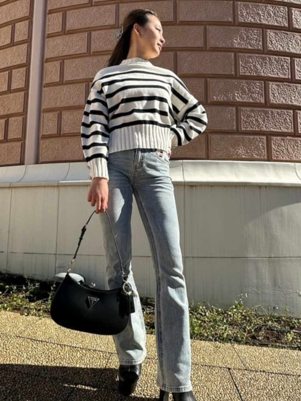 ブラック系のショルダーバッグ、ブルー系のデニムパンツ、ホワイト系のニット/セーターを着用したレディースの春コーディネートの1枚目の写真