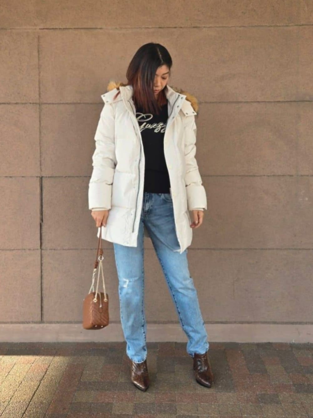 ブルー系のデニムパンツ、ブラック系のTシャツ/カットソー、ブラウン系のショルダーバッグを着用したレディースの冬コーディネートの1枚目の写真