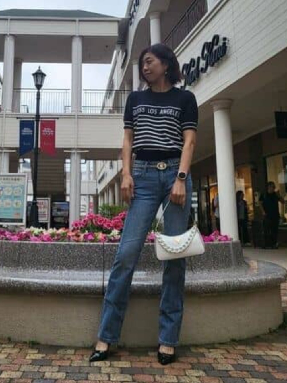 ブルー系のデニムパンツ、ホワイト系のハンドバッグを着用したレディースの春コーディネートの1枚目の写真