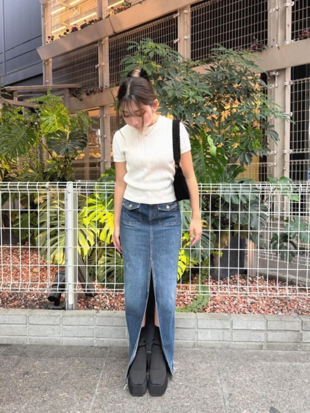 ブルー系のデニムスカート、ホワイト系のニット/セーター、ブラック系のショルダーバッグを着用したレディースの秋コーディネートの1枚目の写真