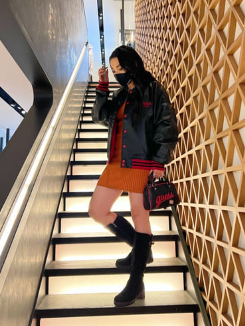 ブラック系のブルゾン、ブラック系のハンドバッグ、オレンジ系のワンピースを着用したレディースの秋コーディネートの1枚目の写真