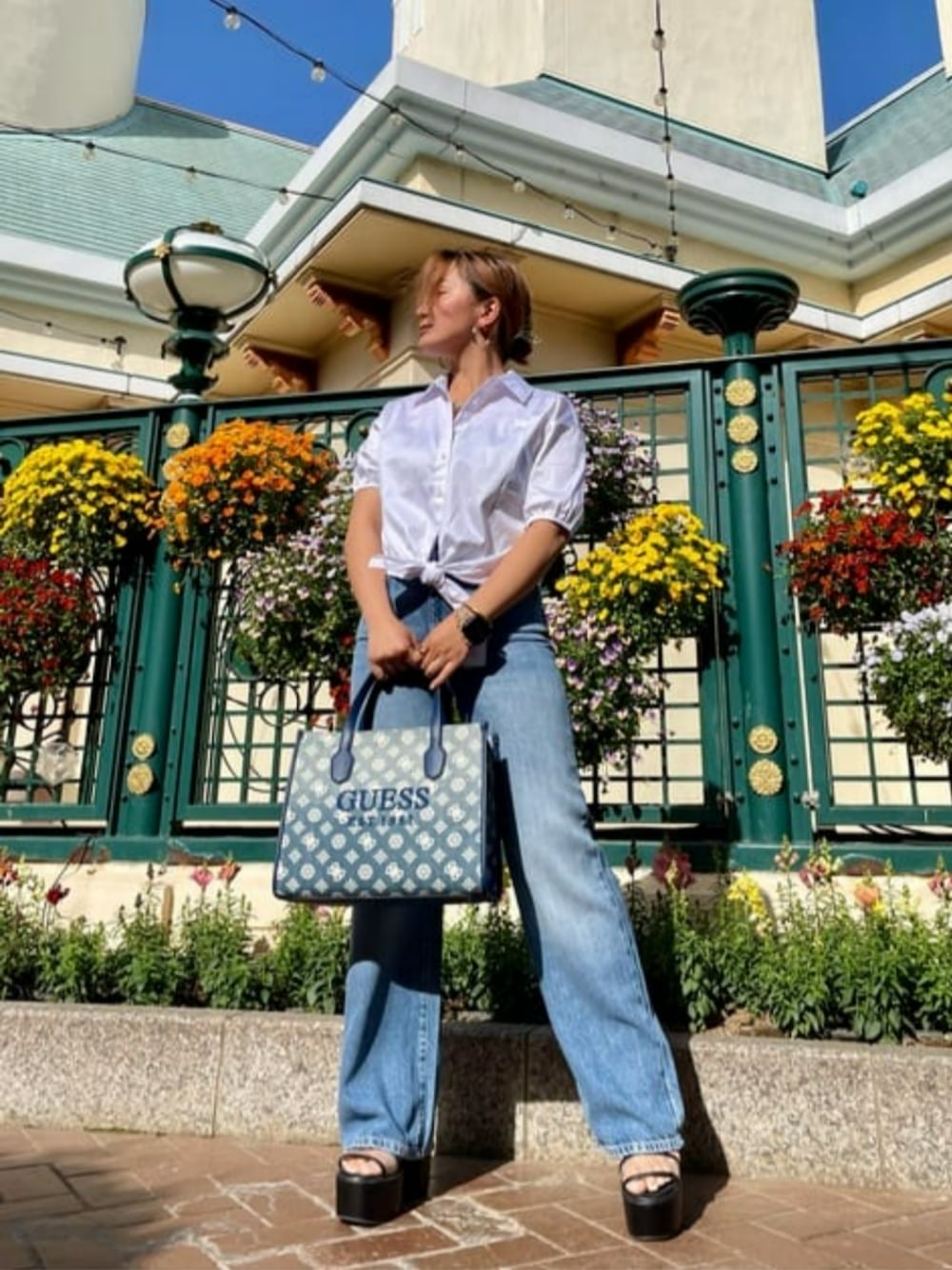ブルー系のデニムパンツ、ホワイト系のシャツ/ブラウス、ブルー系のトートバッグを着用したレディースの夏コーディネートの1枚目の写真