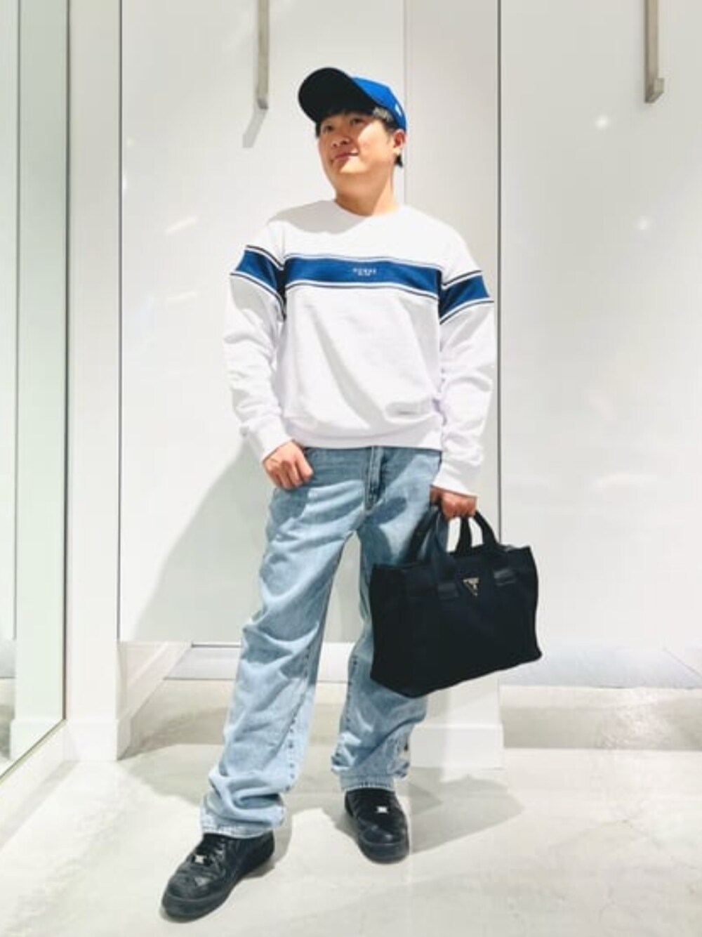 ブルー系のデニムパンツ、ホワイト系のスウェット、ブラック系のトートバッグを着用したメンズの春コーディネートの1枚目の写真