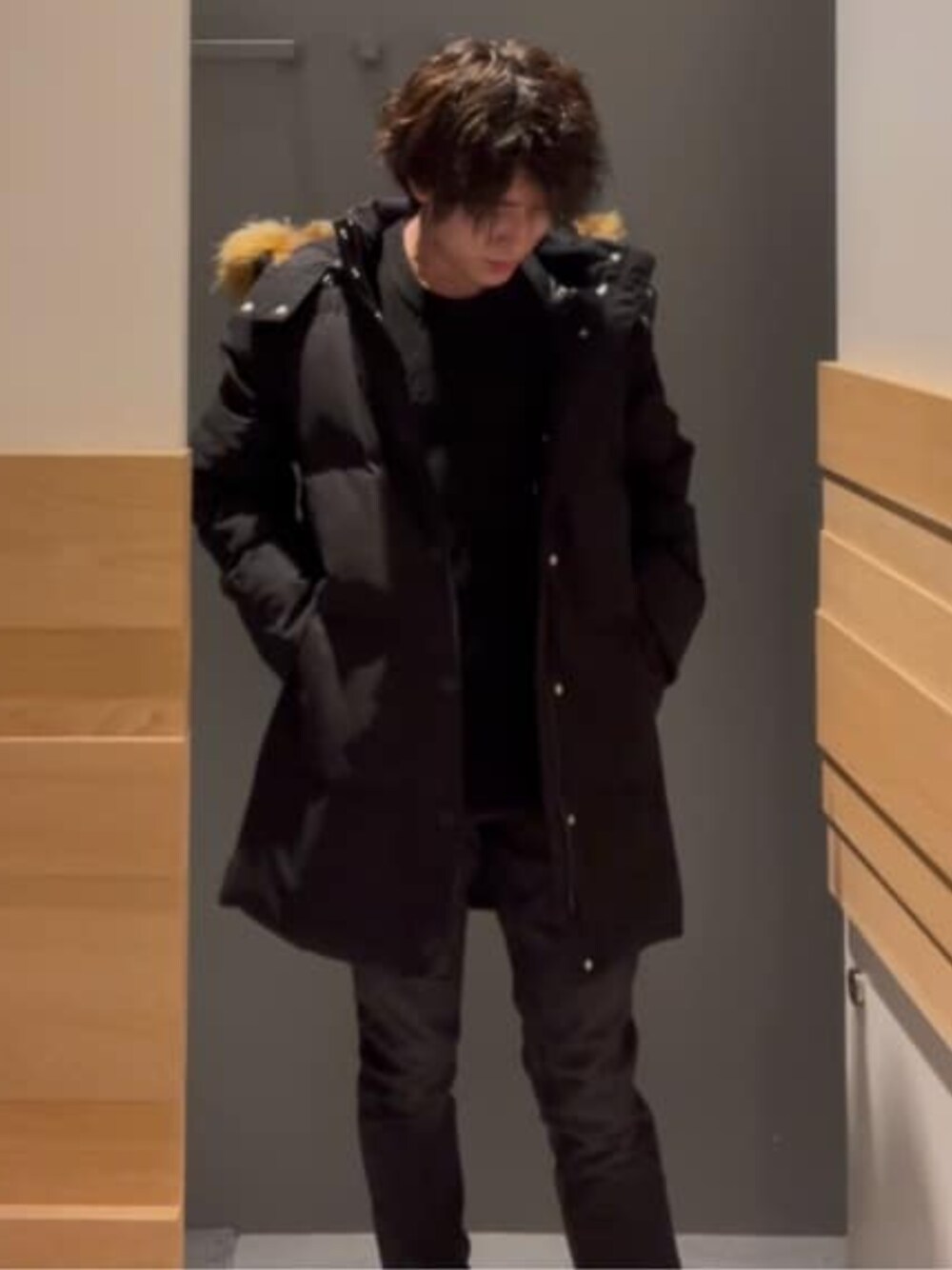 グレー系のデニムパンツ、ブラック系のニット/セーター、ブラック系のダウンジャケット/コートを着用したメンズの冬コーディネートの1枚目の写真