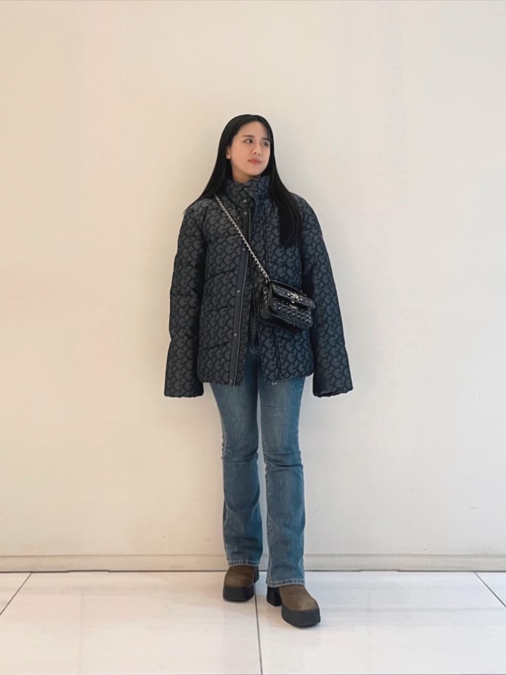 ブルー系のデニムパンツ、ブラック系のニット/セーター、ブラック系のショルダーバッグを着用したレディースの冬コーディネートの1枚目の写真