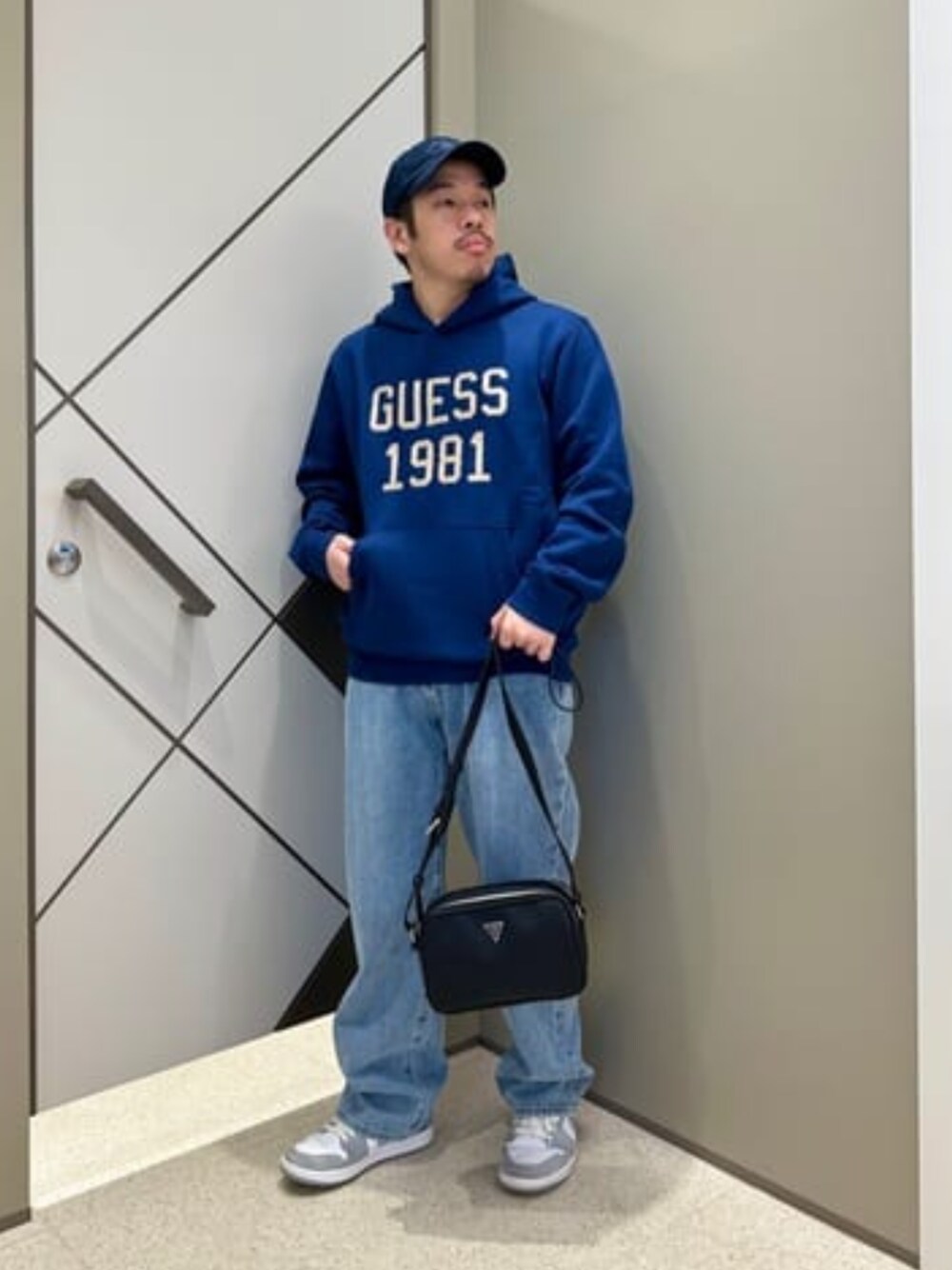 ブルー系のデニムパンツ、ブラック系のショルダーバッグ、ブルー系のパーカーを着用したメンズの秋コーディネートの1枚目の写真