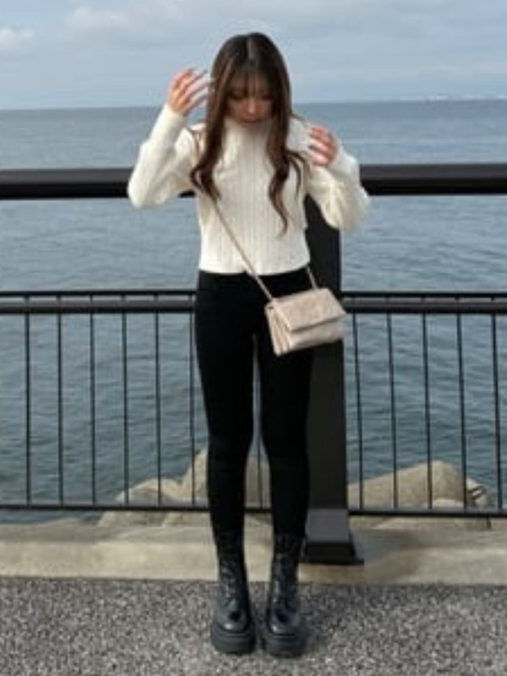ブラック系のデニムパンツ、ベージュ系のショルダーバッグ、ホワイト系のニット/セーターを着用したレディースの冬コーディネートの1枚目の写真