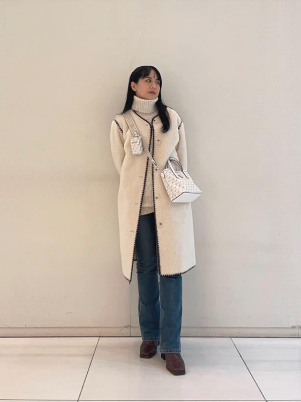 ブルー系のデニムパンツ、ホワイト系のショルダーバッグ、ベージュ系のニット/セーターを着用したレディースの秋コーディネートの1枚目の写真