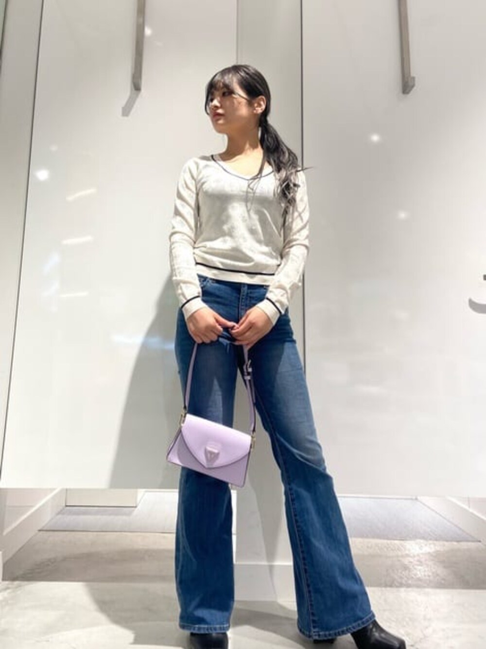 ブルー系のデニムパンツ、ブラック系のショルダーバッグ、ベージュ系のニット/セーターを着用したレディースの春コーディネートの1枚目の写真