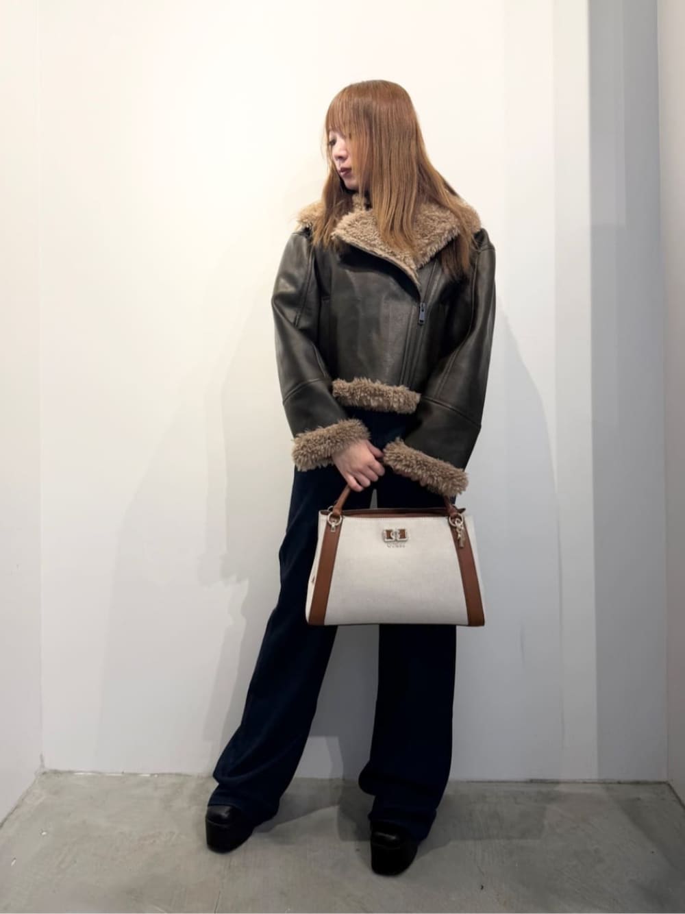 ホワイト系のニット/セーター、イエロー系のハンドバッグ、ブラウン系のライダースジャケットを着用したレディースの冬コーディネートの1枚目の写真