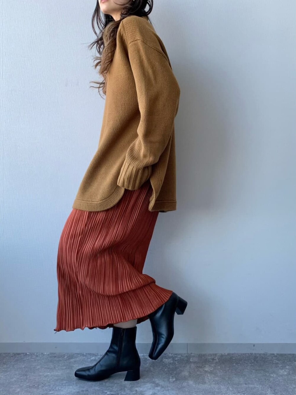 ブラウン系のニット/セーター、レッド系のスカート、ブラック系のブーツを着用したレディースの冬コーディネートの2枚目の写真