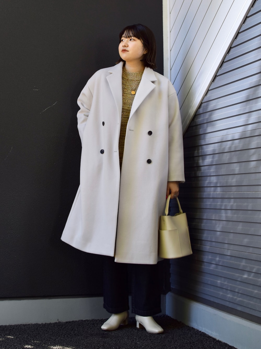 グレー系のチェスターコート、ベージュ系のワンピース、ホワイト系のトートバッグを着用したレディースの秋コーディネートの1枚目の写真