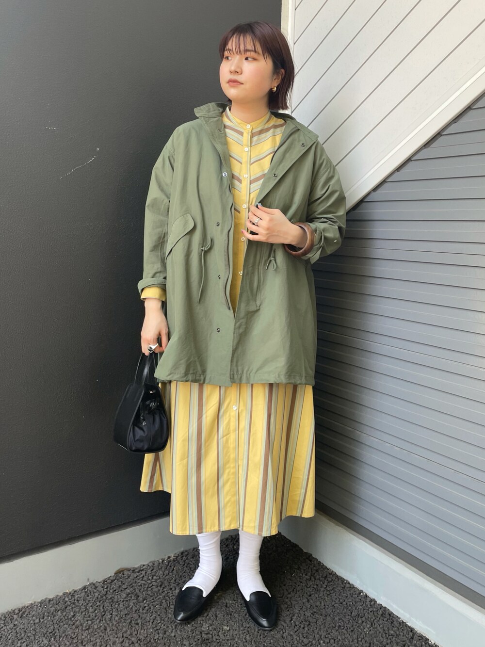 グリーン系のモッズコート、イエロー系のワンピース、ブラック系のスリッポンを着用したレディースの春コーディネートの1枚目の写真