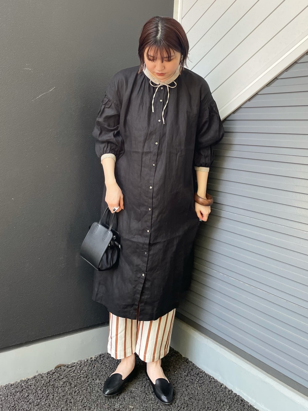 ブラック系のショルダーバッグ、ブラック系のスリッポン、ホワイト系のパンツを着用したレディースの春コーディネートの1枚目の写真