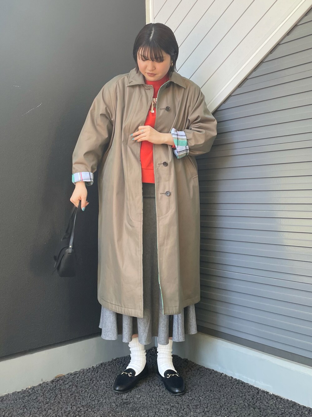 グリーン系のステンカラーコート、グレー系のスカート、ブラック系のショルダーバッグを着用したレディースの冬コーディネートの1枚目の写真