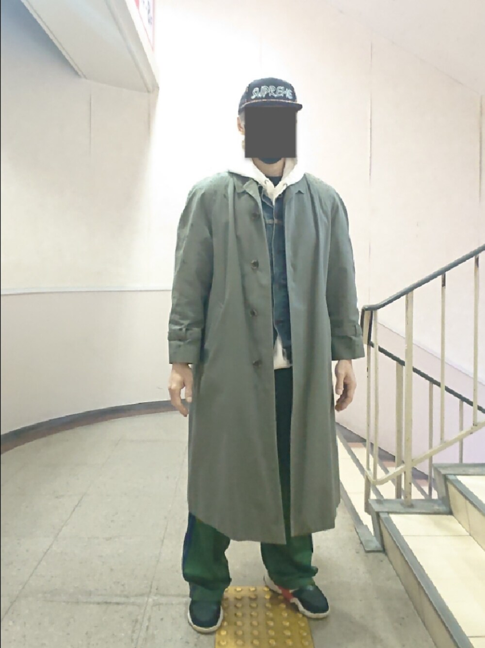 グレー系のステンカラーコート、ブルー系のデニムジャケット、グリーン系のその他パンツを着用したメンズの冬コーディネートの1枚目の写真