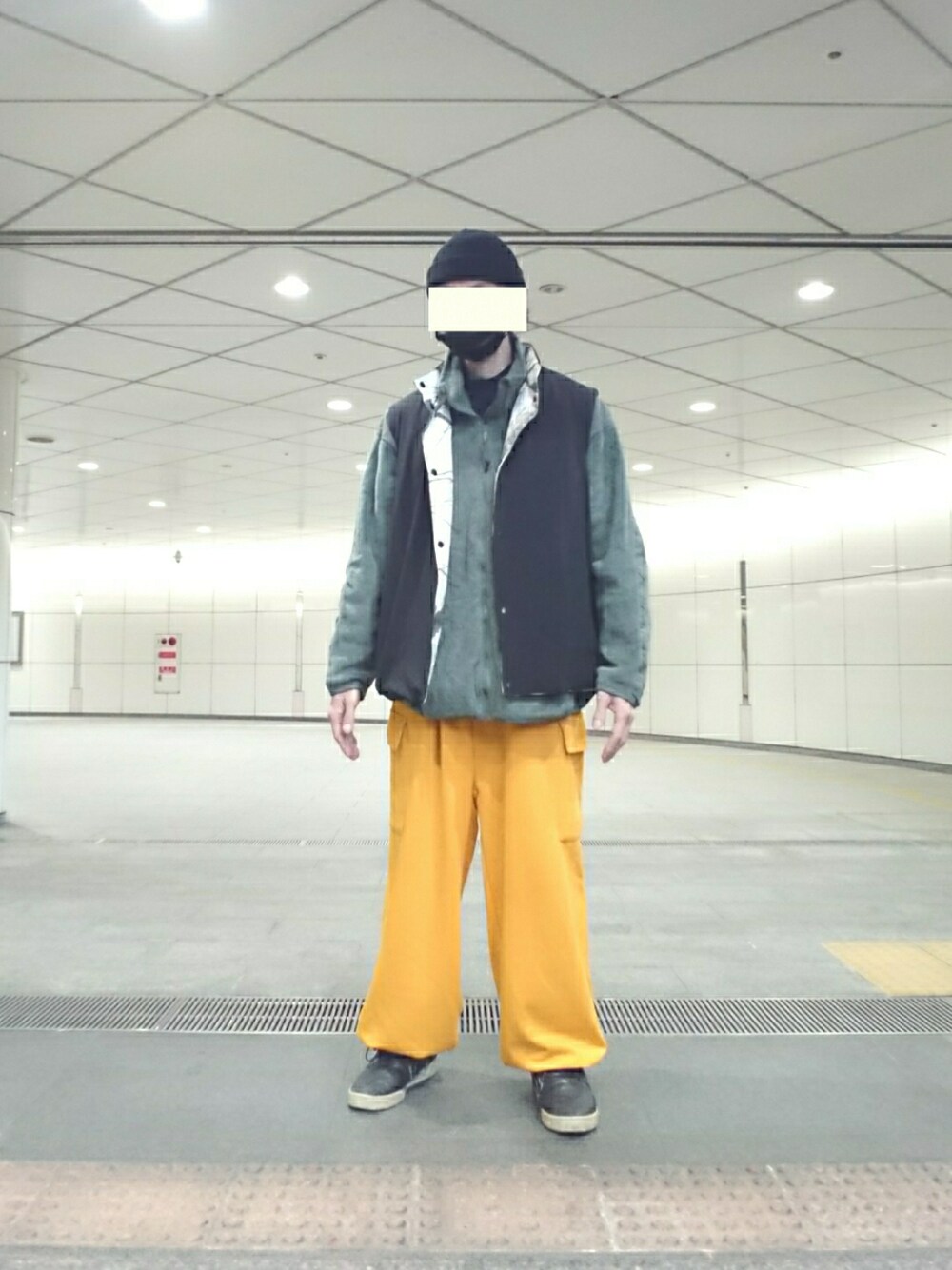 グレー系のミリタリージャケット、ブラック系のダウンベスト、イエロー系のカーゴパンツを着用したメンズの春コーディネートの1枚目の写真