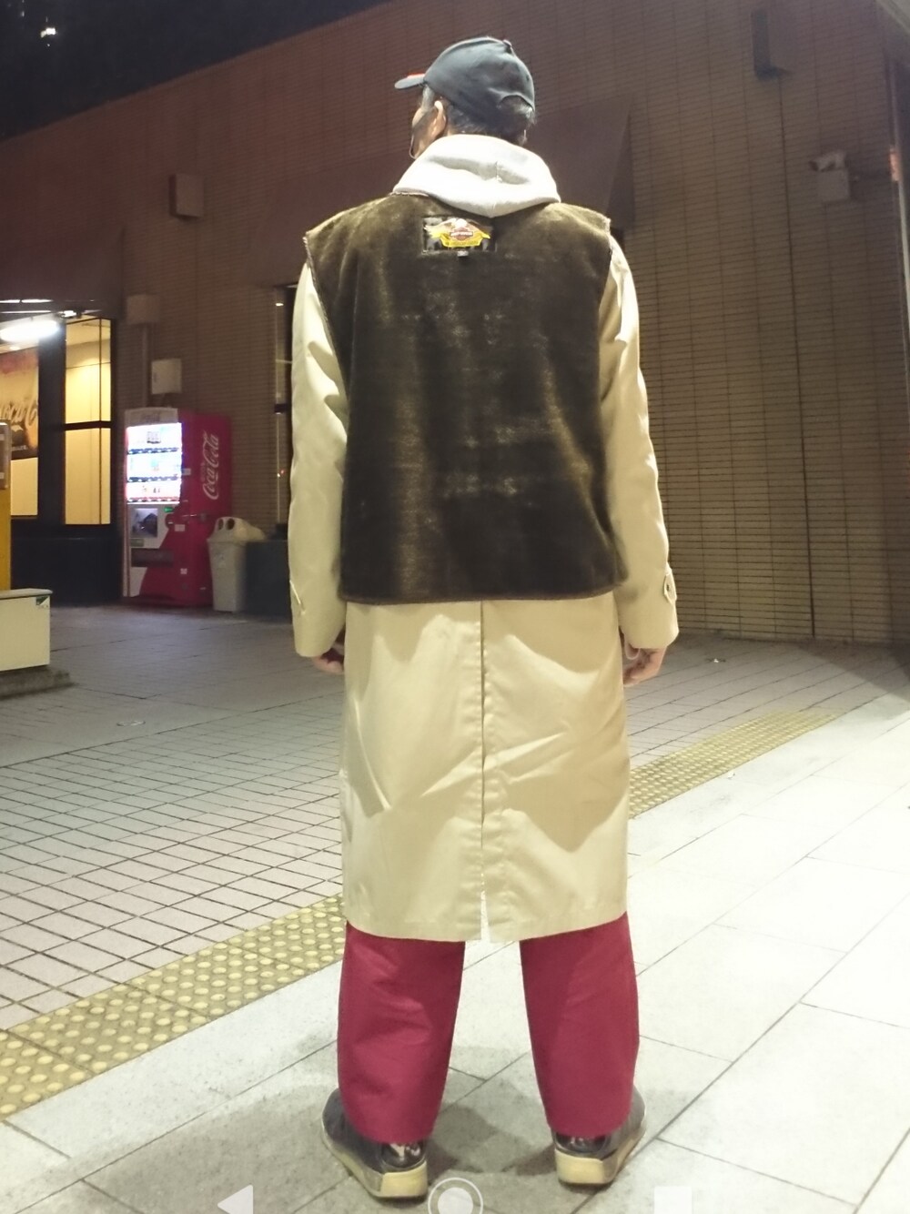 グレー系のパーカー、ブラウン系のベスト、ベージュ系のステンカラーコートを着用したメンズの春コーディネートの2枚目の写真