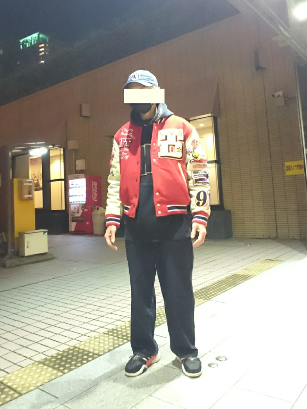 レッド系のスタジャン、ブラック系のパーカー、ブルー系のデニムパンツを着用したメンズの冬コーディネートの1枚目の写真