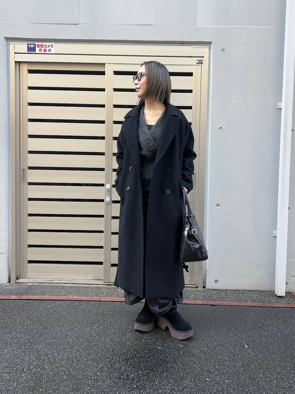 ブラック系のチェスターコート、ブラック系のスカート、グレー系のカーディガン/ボレロを着用したレディースの冬コーディネートの1枚目の写真