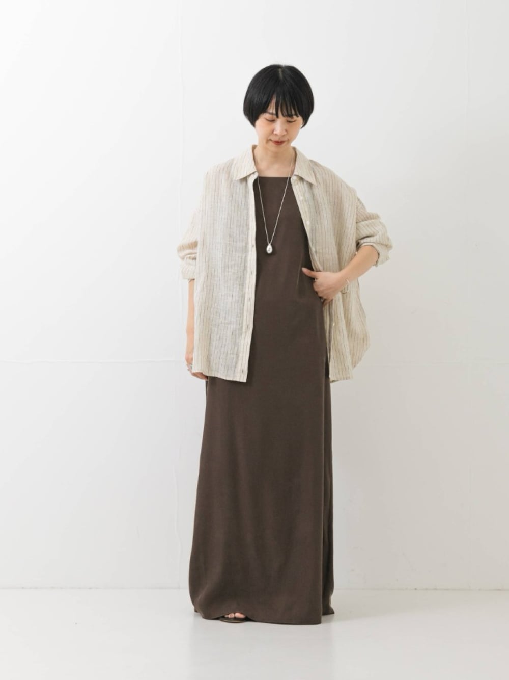 ブラウン系のワンピース、ベージュ系のシャツ/ブラウス、シルバー系のネックレスを着用したレディースの夏コーディネートの1枚目の写真