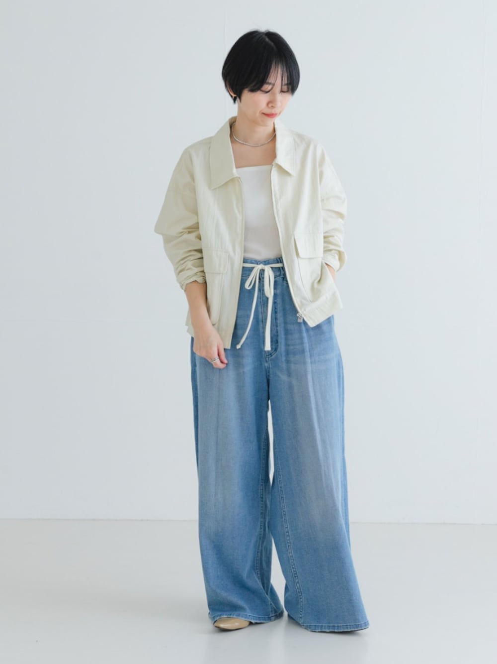 ベージュ系のパンプス、ホワイト系のブルゾン、ブルー系のデニムパンツを着用したレディースの春コーディネートの1枚目の写真