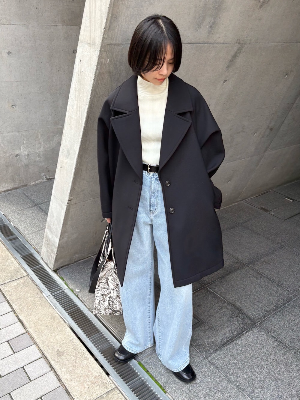 ブラック系のチェスターコート、ホワイト系のニット/セーター、ブラック系のローファーを着用したレディースの冬コーディネートの1枚目の写真