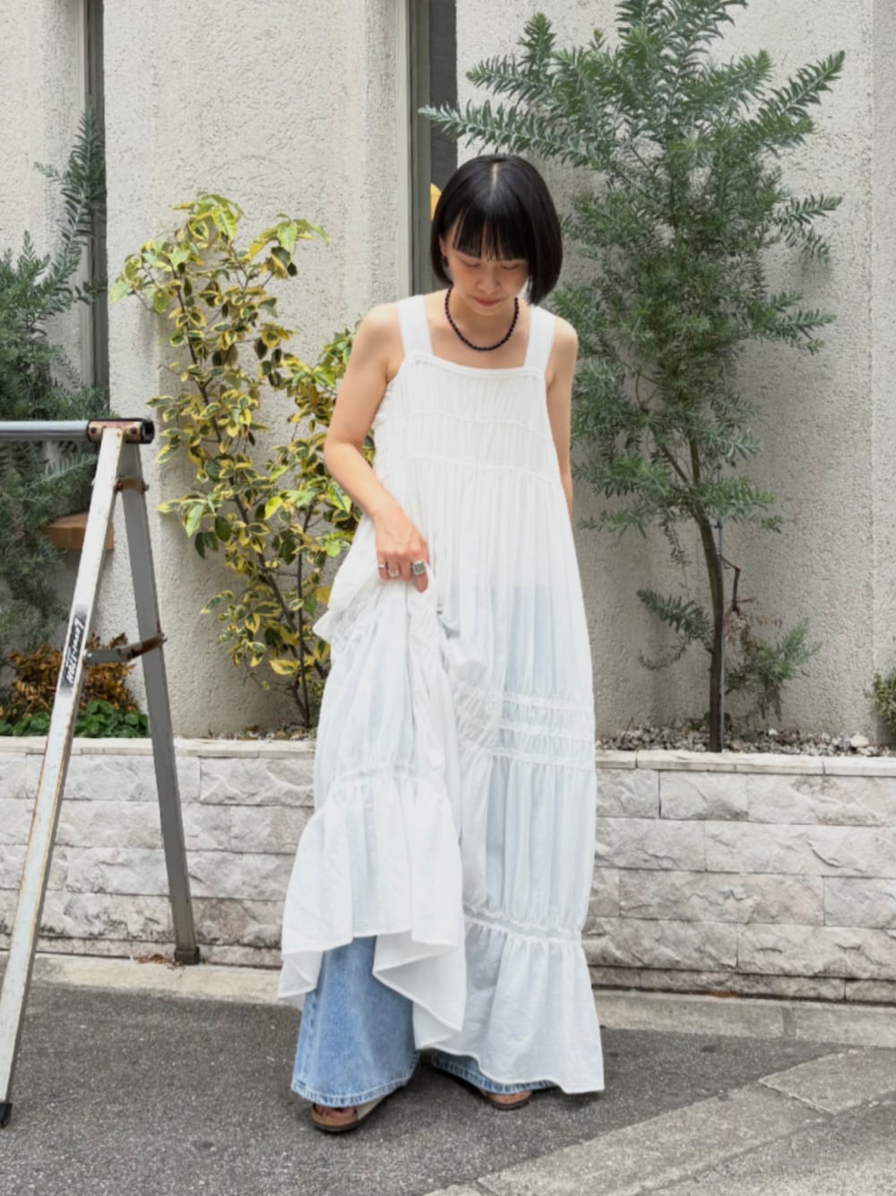 ホワイト系のワンピース、ブルー系のデニムパンツ、ベージュ系のサンダルを着用したレディースの夏コーディネートの1枚目の写真