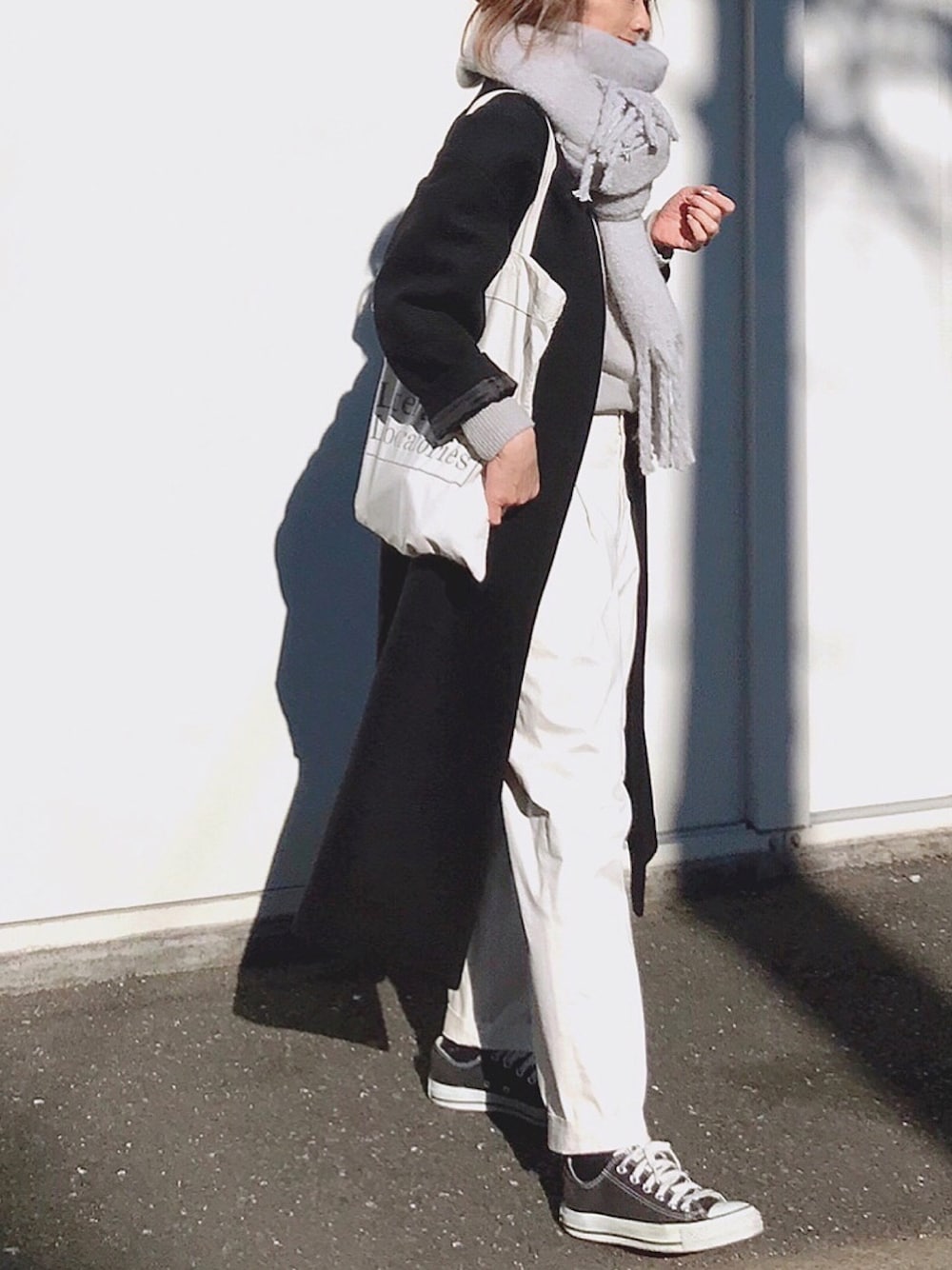 ブラック系のスニーカー、ホワイト系のトートバッグ、ブラック系のノーカラーコートを着用したレディースの冬コーディネートの1枚目の写真