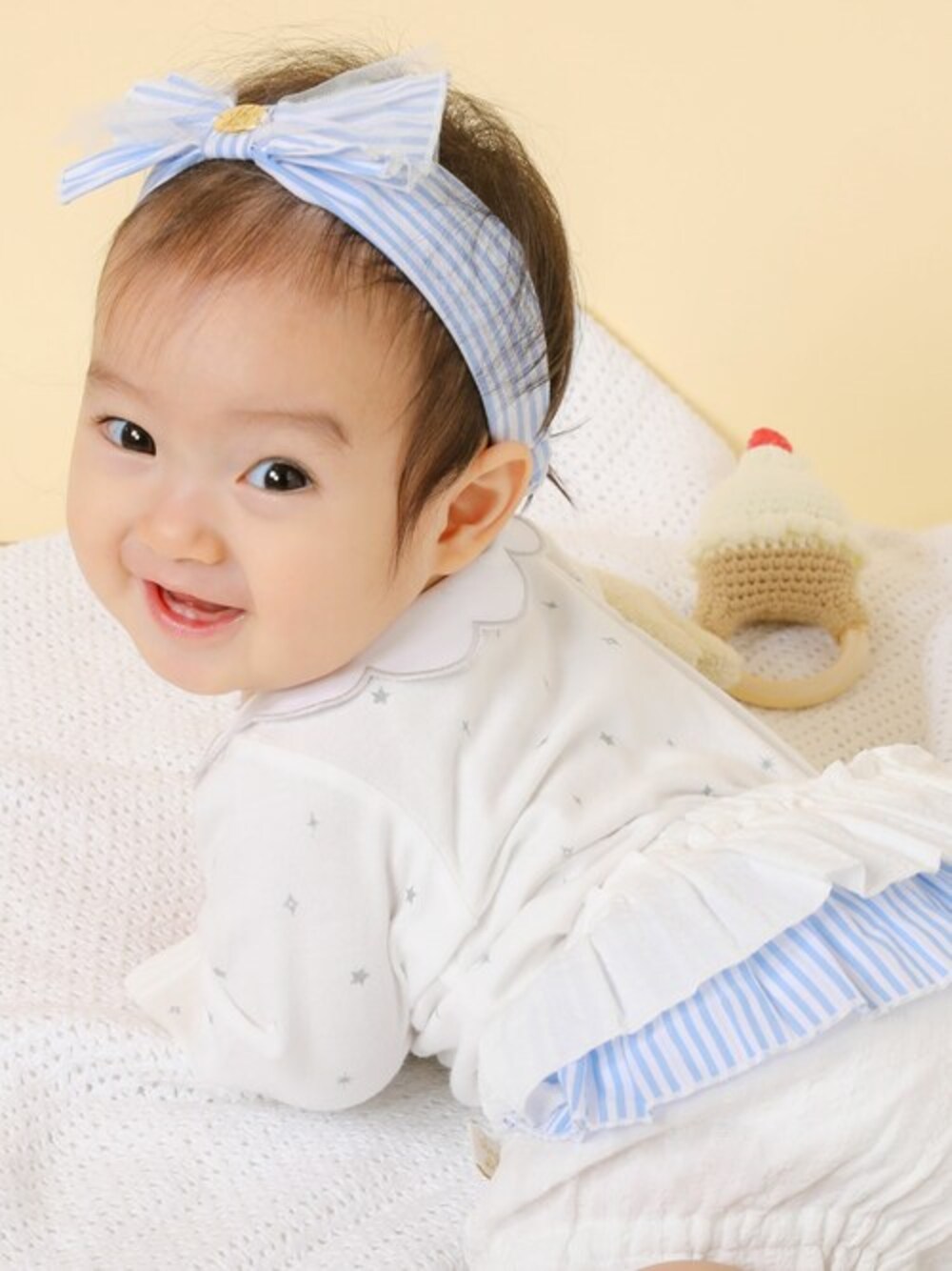 ホワイト系のロンパース、ホワイト系のその他ベビー用品、ブルー系のヘアバンドを着用したキッズの春コーディネートの1枚目の写真