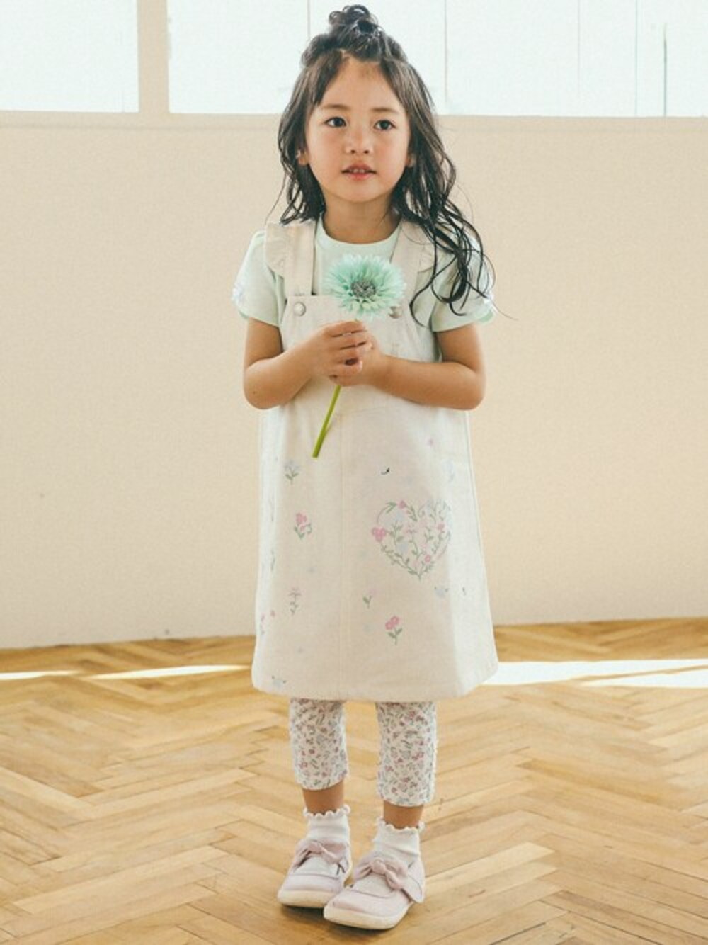 グリーン系のTシャツ/カットソー、ホワイト系のジャンパースカート、パープル系のレギンス/スパッツを着用したキッズの春コーディネートの1枚目の写真