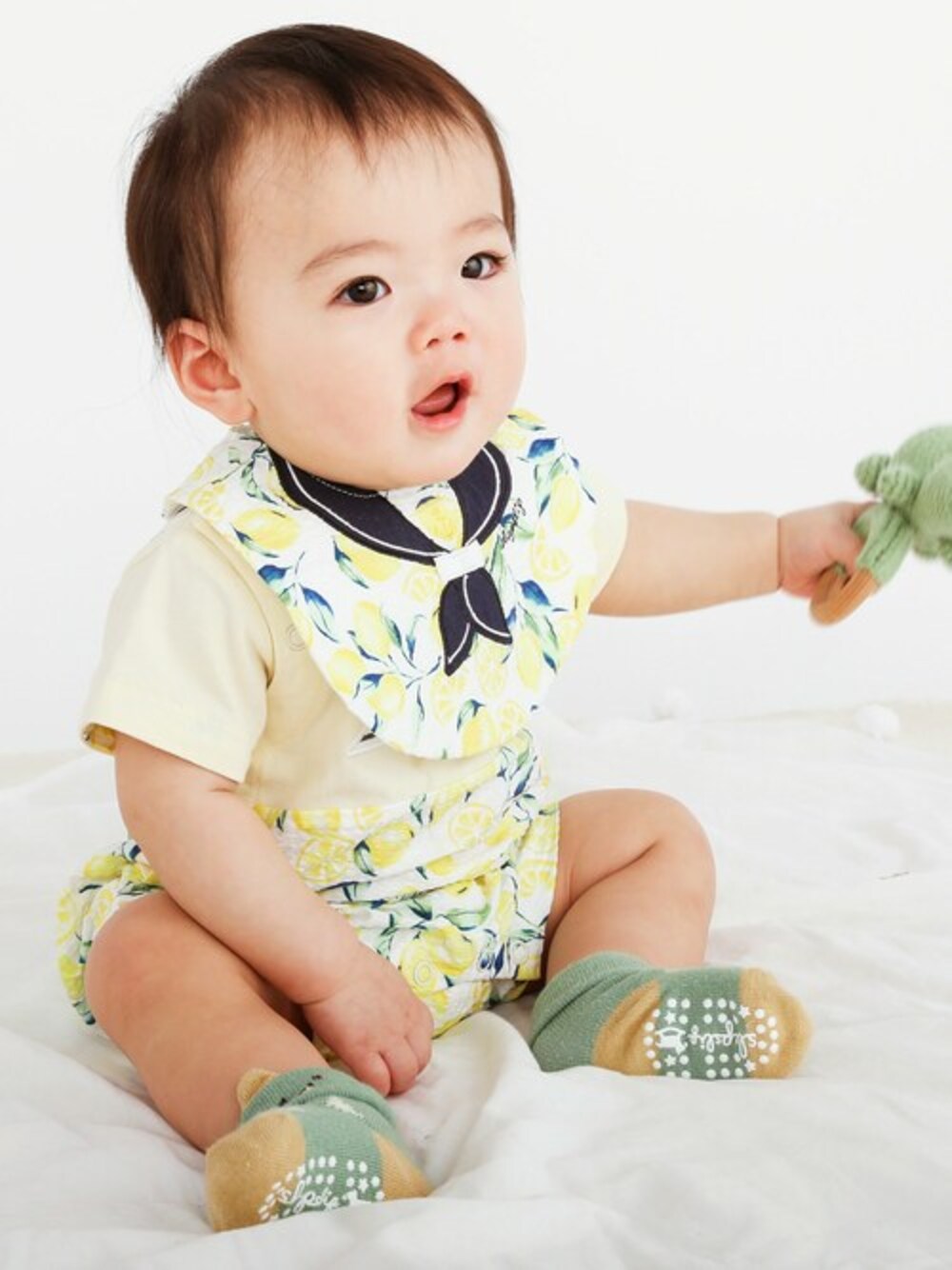 イエロー系のスタイ/よだれかけ、イエロー系のロンパース、グリーン系のその他ベビー用品を着用したキッズの春コーディネートの1枚目の写真