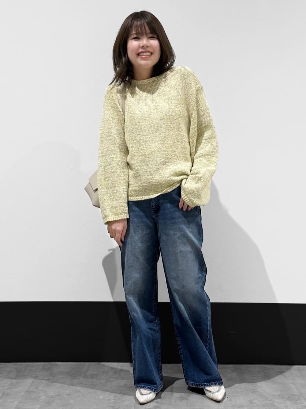 イエロー系のニット/セーター、ブルー系のデニムパンツ、ベージュ系のショルダーバッグを着用したレディースの春コーディネートの1枚目の写真