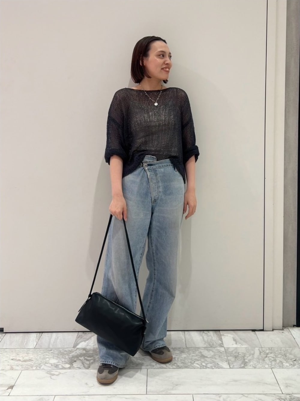 グレー系のニット/セーター、ブルー系のデニムパンツ、ブラック系のハンドバッグを着用したレディースの秋コーディネートの1枚目の写真