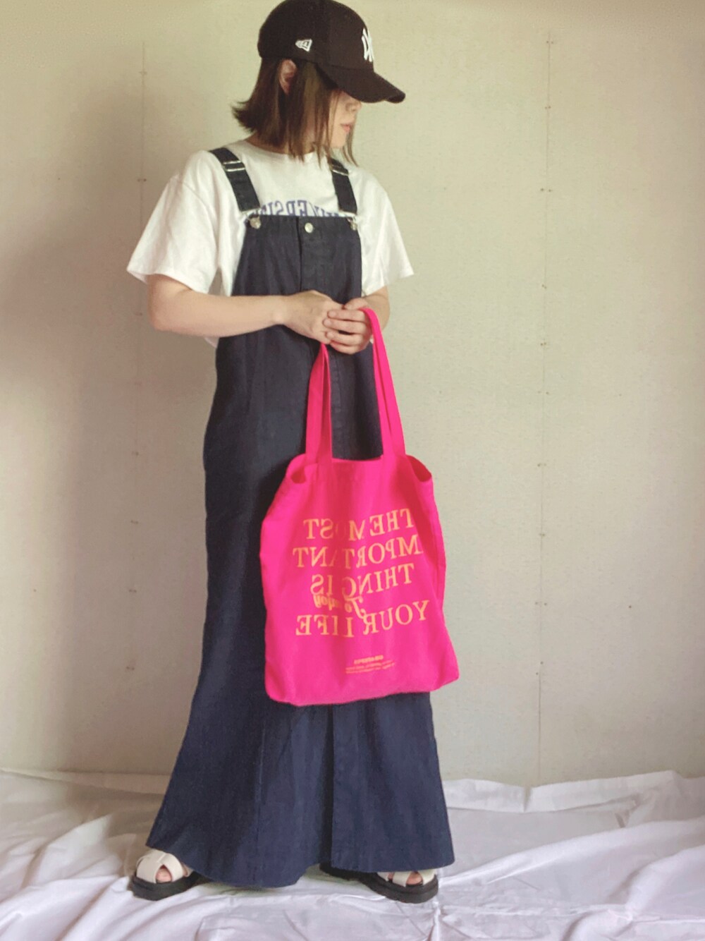 ブルー系のジャンパースカート、ホワイト系のTシャツ/カットソー、ピンク系のトートバッグを着用したレディースの夏コーディネートの1枚目の写真